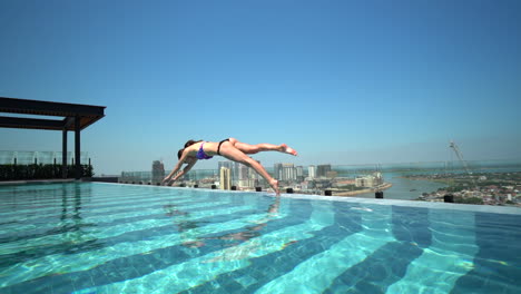 Woman-diving-into-a-rooftop-infinity-pool-in-slow-motion-overlooking-the-Mekong-River-in-downtown-Phnom-Pehn,-Cambodia