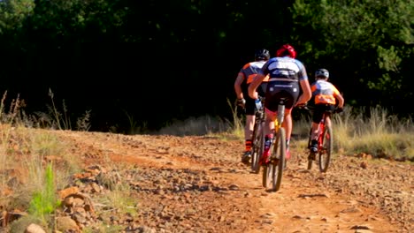 Tres-Ciclistas-De-Montaña-Ocupados-Escalando-Un-Paso-De-Montaña-De-Camino-De-Ripio