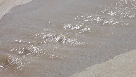 River-running-into-the-ocean,-creating-a-weird-sand-channel-into-the-major-body-of-water