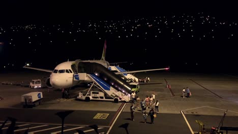 Aterrizaje-Del-Avión-Pasajeros-Que-Salen-Del-Avión-De-Llegada,-Desembarque-Operación-Nocturna-Del-Aeropuerto,-La-Escalera-Pbb-Se-Mueve-Hacia-El-Avión-Para-Apoyar-La-Salida-Segura-De-Descarga-Luces-Del-Cielo-Oscuro