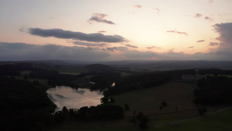 Fallende-Luftaufnahme-Eines-Landguts-Und-Sees-Während-Des-Sonnenuntergangs