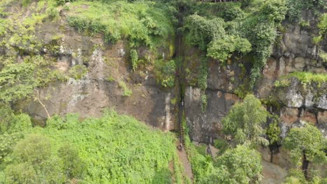 Aerial-shot-orbiting-around-a-African-men-climbing-a-dangerous-ladder-up-a-cliff-in-a-jungle-valley