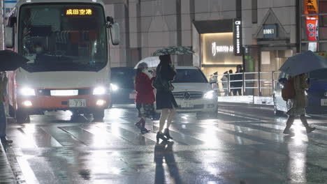 Gente-Con-Paraguas-Cruzando-La-Calle-En-Una-Noche-Lluviosa-Con-Vehículos-En-El-Fondo-En-Shinjuku,-Tokio,-Japón