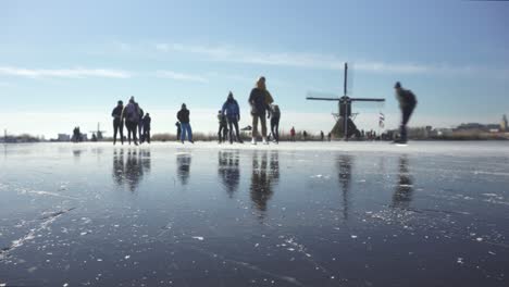 Holländische-Einheimische-Beim-Schlittschuhlaufen-Auf-Zugefrorenen-Kanälen-Im-Polderland-In-Der-Nähe-Von-Windmühlen