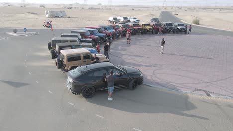 Car-bloggers-on-off-road-event-meeting-on-Dubai-desert,-aerial-arc-shot