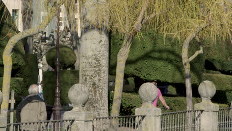 People-walking-and-cycling-in-Paseo-Espolon,-Burgos,-Spain,-wide-shot-slowmo