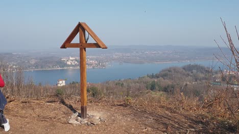 Old-woman-with-wooden-sticks-for-trekking-next-cross-at-Motta-Grande-viewpoint-at-Arona,-Italy