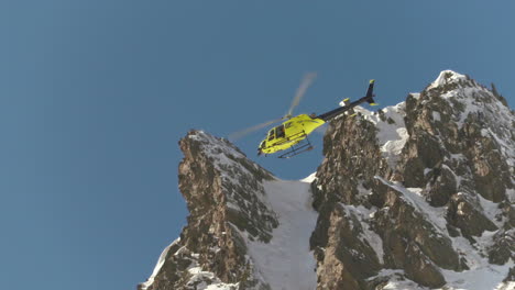 Rescue-helicopter-flying-over-a-snowy-mountain,-during-the-Freeride-Wolrd-Tour-competition,-in-Andorra