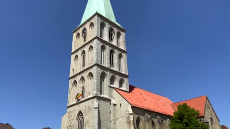 Tilt-up-shot-of-historic-german-cathedral-with-waving-rainbow-flag-during-sunny-day-and-blue-sky