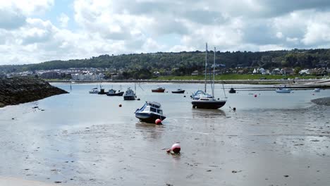 Aerial-view-moored-boats-on-Welsh-low-tide-seaside-breakwater-harbour-coastline-low-push-in-right