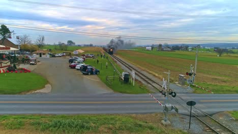 Una-Vista-Aérea-De-Un-Antiguo-Tren-De-Vapor-Restaurado-Y-Vagones-De-Pasajeros-Que-Se-Acercan-Con-Humo-Y-Vapor-Con-Turistas-Y-Espectadores-Mirando-Como-Los-Ve-Un-Dron