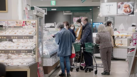 Kunden,-Die-In-Einem-Supermarkt-Eine-Maske-Tragen-Und-Während-Einer-Pandemie-In-Tokio,-Japan,-Tiefkühlkost-Auf-Einer-Glasvitrine-Auswählen