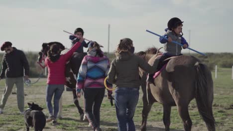 Los-Niños-Se-Sientan-En-La-Parte-Superior-Del-Caballo-Con-La-Ayuda-De-Entrenadores-De-Caballos-En-Un-Día-Soleado-En-Argentina