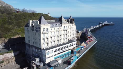 Aerial-view-of-The-Grand-hotel-landmark-Llandudno-seafront-seaside-Victorian-promenade-tourism-building-rising-tilt-down