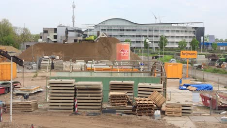 Zeitraffer-Für-Schwere-Maschinen-Mit-Großem-Bagger,-Der-Sand-In-Einem-Großen-Haufen-Auf-Einer-Baustelle-Für-Zukünftige-Gebäude-Mit-Windmühlen-Im-Hintergrund-Verschiebt