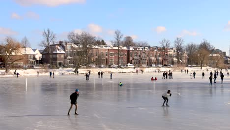 Ice-skating-people-slow-panning-movement-in-picturesque-urban-scenery-on-frozen-canal-in-city-environment-with-winter-barren-trees-and-white-snow-in-cold-cozy-landscape