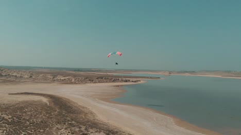 Aerial-View-Of-Motorised-Paraglider-Flying-Over-Arid-Coastline-Next-To-Salt-Lake