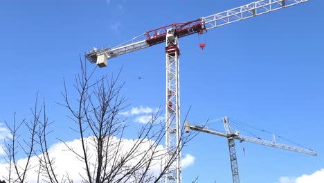 Couple-of-tall-steel-construction-cranes-isolated-on-blue-sky,-motion-view