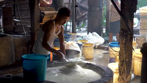 Traditional-tofu-factory-employee-gathers-and-throw-out-froth-from-soy-mixture