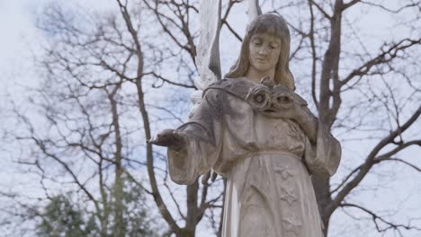 Statue-of-Marble-Angel-with-Cracked-Face-with-Tree-Branches-in-Background