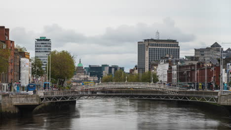 Zeitraffer-Des-Liffey-Flusses-Mit-Menschen,-Die-Die-Brücke-überqueren,-Und-Tagsüber-Verkehr-Und-Architektur-Am-Flussufer-In-Der-Stadt-Dublin-In-Irland