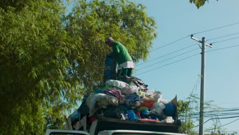 Garbage-collector-stands-on-top-of-truck-filled-with-rubbish
