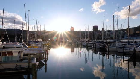 Yachts-and-boats-berthed-in-the-city-waterfront-harbour-marina,-beautiful-sunny-afternoon,-sun-rays,-reflections,-blue-skies-and-cityscape-of-Wellington,-New-Zealand