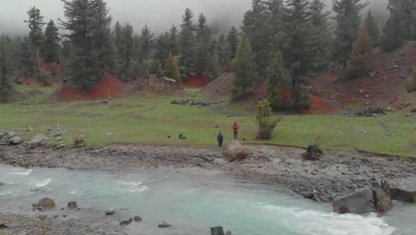 Aerial-View-Of-Friends-Next-To-Naltar-River-Bank-In-Valley