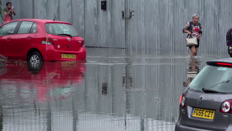 Two-women-wade-through-floodwater,-past-two-submerged-cars-following-thunderstorms-that-saw-more-than-a-month’s-worth-of-torrential-rain-fall-in-several-hours-across-the-capital