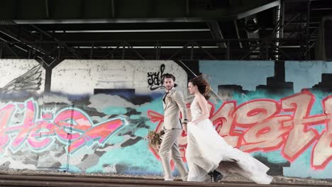 Urban-styled-wedding-couple-in-boots-and-sneaker-running-along-train-rails-and-graffit-urban-environment-escaping