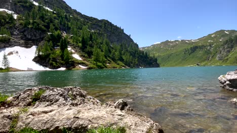 Panorama-shot-of-idyllic-mountain-river-surrounded-by-green-mountains-and-snow-on-river-shore---Climate-change-and-global-warming