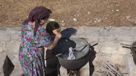 Una-Mujer-Vierte-Agua-Caliente-En-Una-Caldera-De-Xartzin-O-Cobre-Durante-Una-Recreación-Histórica-Del-Lavado-De-Ropa-Como-Lo-Hacían-En-1900-En-Kritou-Terra,-Grecia