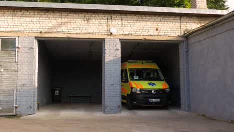 Vehículo-De-Ambulancia-Paramédico-Amarillo-Estacionado-Dentro-Del-Garaje-De-Ladrillo-Blanco,-Día-Soleado,-Plano-General