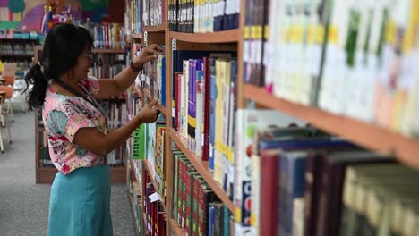 Bibliotecaria,-Mujer-Asiática-Con-Anteojos,-Toma-Alegremente-Un-Libro-Del-Estante