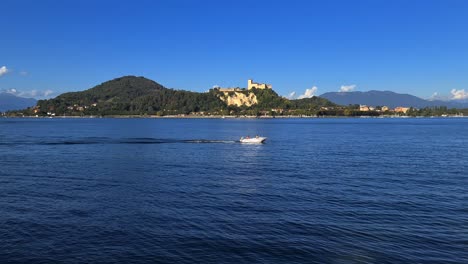 Small-motorboat-navigating-in-calm-lake-waters-of-Maggiore-lake-in-Italy-with-Angera-castle-in-background