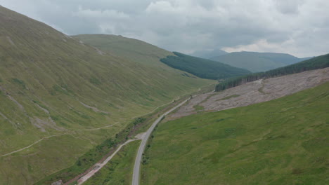 High-wide-dolly-forward-drone-shot-of-road-through-Scottish-highlands-Scotland