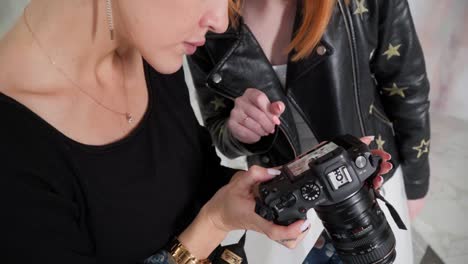 Ladies-looking-through-pictures-on-a-camera-during-a-photoshoot,-photographer-and-a-model-take-pictures-indoors-in-a-studio,-smiling-and-enjoying-the-result