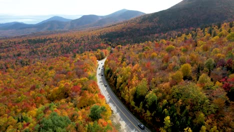 Aerial-view-of-cars-driving-through-forest-in-New-England-during-fall