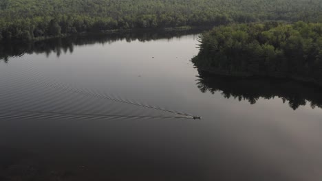 Static-aerial-shot-over-flat-calm-lake-lake-boat-travels-across-surface-surrounded-by-wilderness
