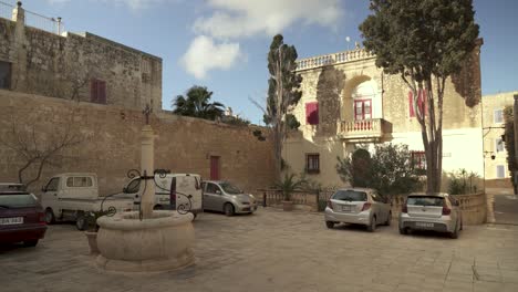 Cars-Parked-Outside-Ancient-House-with-Trees-and-Palm-Waving-in-the-Wind-in-Mdina