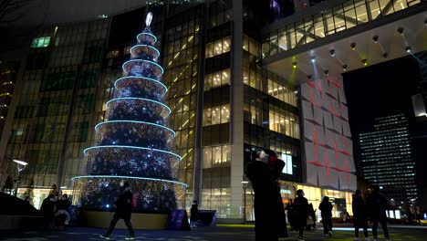 People-wearing-face-masks-at-a-Christmas-lights-display-outside-the-Lotte-World-Tower-at-night-in-Seoul,-South-Korea