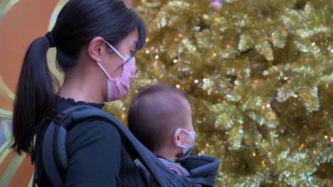 Eine-Mutter-Und-Ihr-Baby-Stehen-Schlange,-Um-Einen-Abend-Bei-Einer-Weihnachtlichen-Installationsveranstaltung-Mit-Goldenen-Weihnachtsbäumen-Und-Verschiedenen-Ornamenten-Und-Dekorationen-In-Hongkong-Zu-Genießen