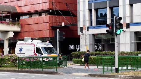 An-emergency-medical-response-vehicle-driving-on-hill-street-with-flashy-lights-and-sirens,-waited-at-the-traffic-lights-at-busy-metropolitan-area,-Singapore-Asia