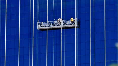 Two-maintenance-workers-on-mechanical-hoist-perform-tasks-on-the-glass-facade-of-a-commercial-building-in-Cebu-City