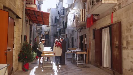 Woman-on-a-street-stand-selling-products-on-a-narrow-beautiful-street-in-Bari,-Italy