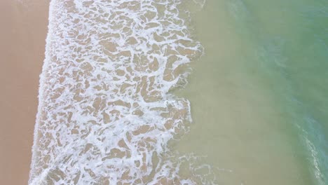 Aerial-forward-tilt-up-reveal-of-waves-breaking-on-St-Ives-beach,-Cornwall