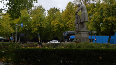 Plano-General-Del-Parque-De-Otoño-Con-La-Estatua-De-Christopher-Polhem-Y-El-Tráfico-En-La-Carretera-En-El-Fondo--gotemburgo,-Suecia