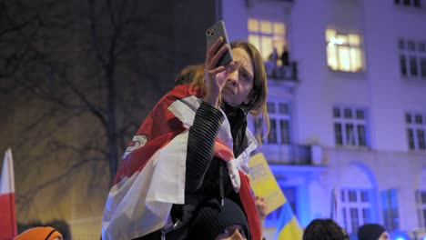 2022-Invasión-Rusa-De-Ucrania---Niña-Con-Una-Bandera-De-Bielorrusia-Libre-Filmando-Con-Su-Teléfono-En-Una-Manifestación-Contra-La-Guerra-En-Varsovia-El-Primer-Día-De-La-Guerra