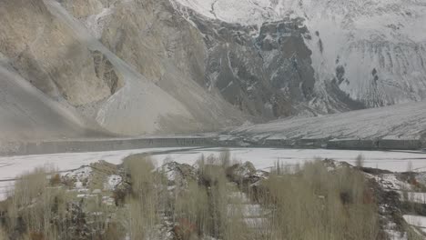 Aerial-Over-Winter-Trees-To-Reveal-Frozen-Lake-Attabad-Lake-In-Hunza-Valley-With-Snow-Capped-Mountains-In-Background