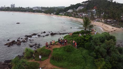 Aerial-dolly-out-rising-over-people-having-fun-in-Pigeon-Island-rocky-sea-shore-surrounded-by-vegetation,-Sri-Lanka